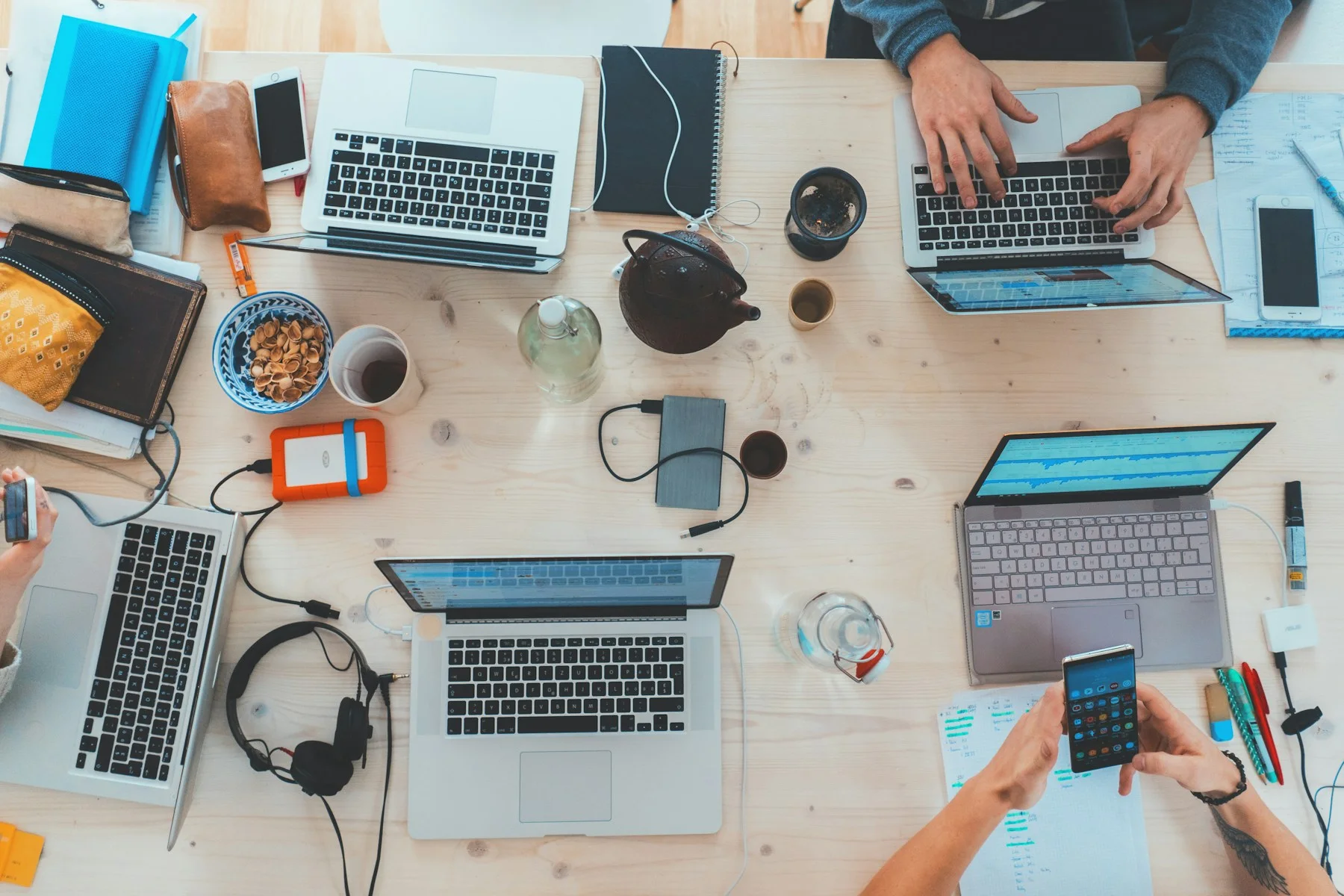 A shared work surface with laptops, notes and people collaborating